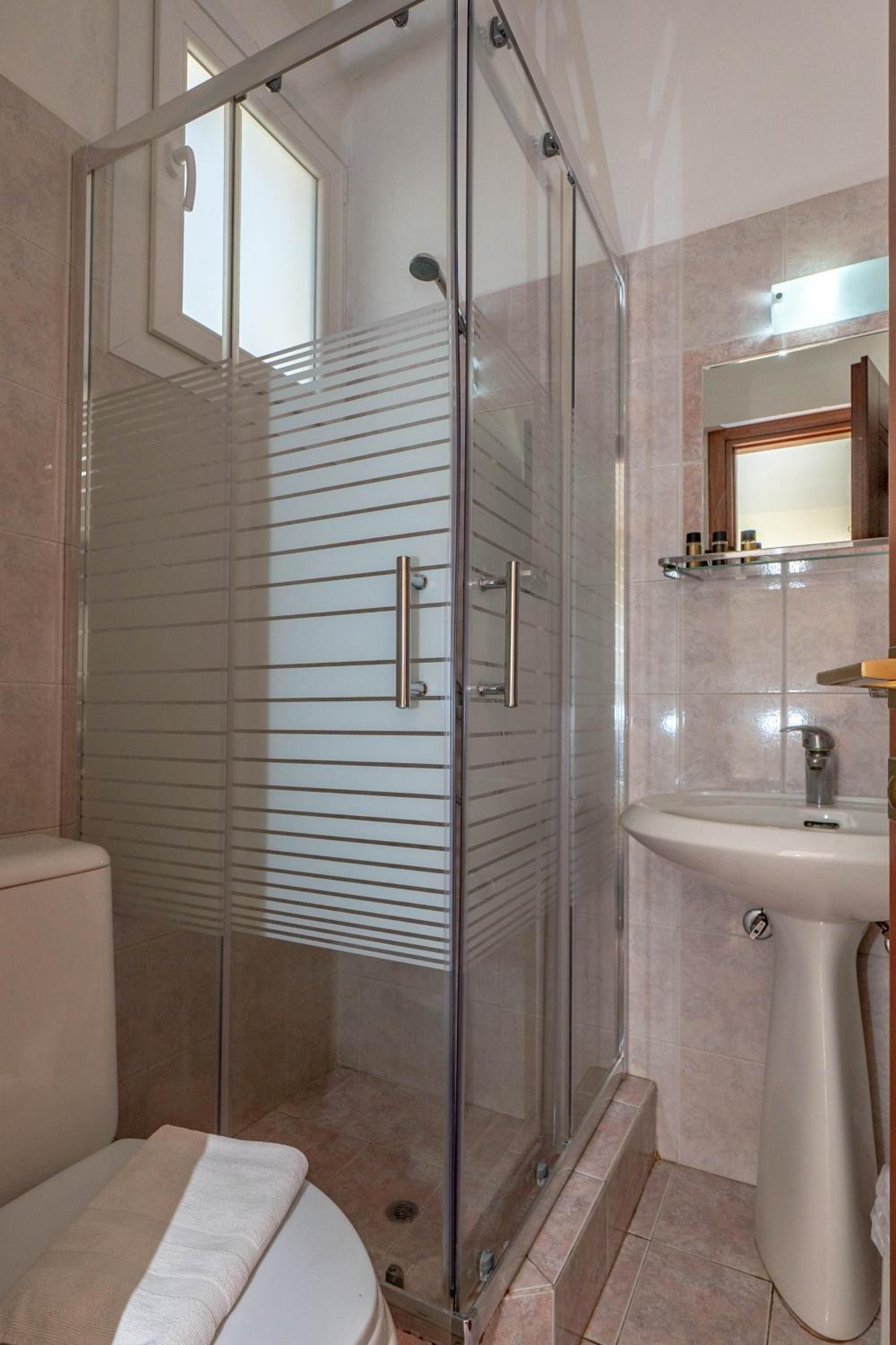 A bathroom with a glass shower enclosure, a toilet, and a sink with a mirror above it.