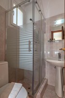 Un baño con cabina de ducha de vidrio, inodoro y lavamanos con espejo.