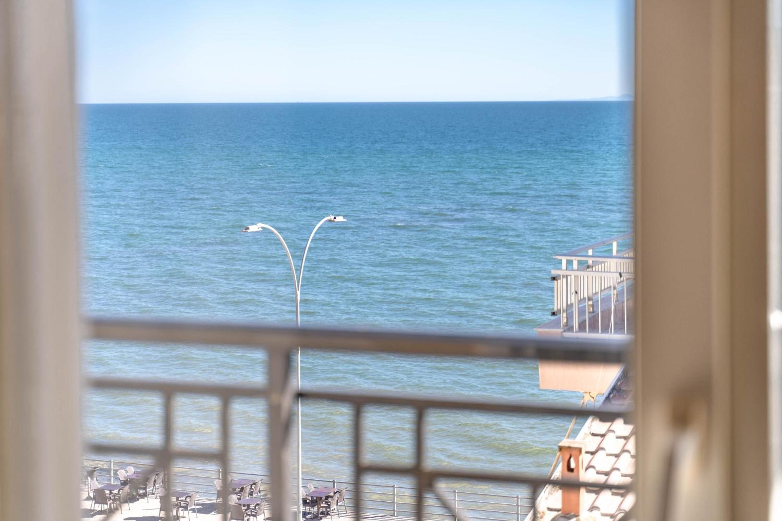 Vista del mar desde un balcón con barandilla, una farola y un edificio también con balcón.