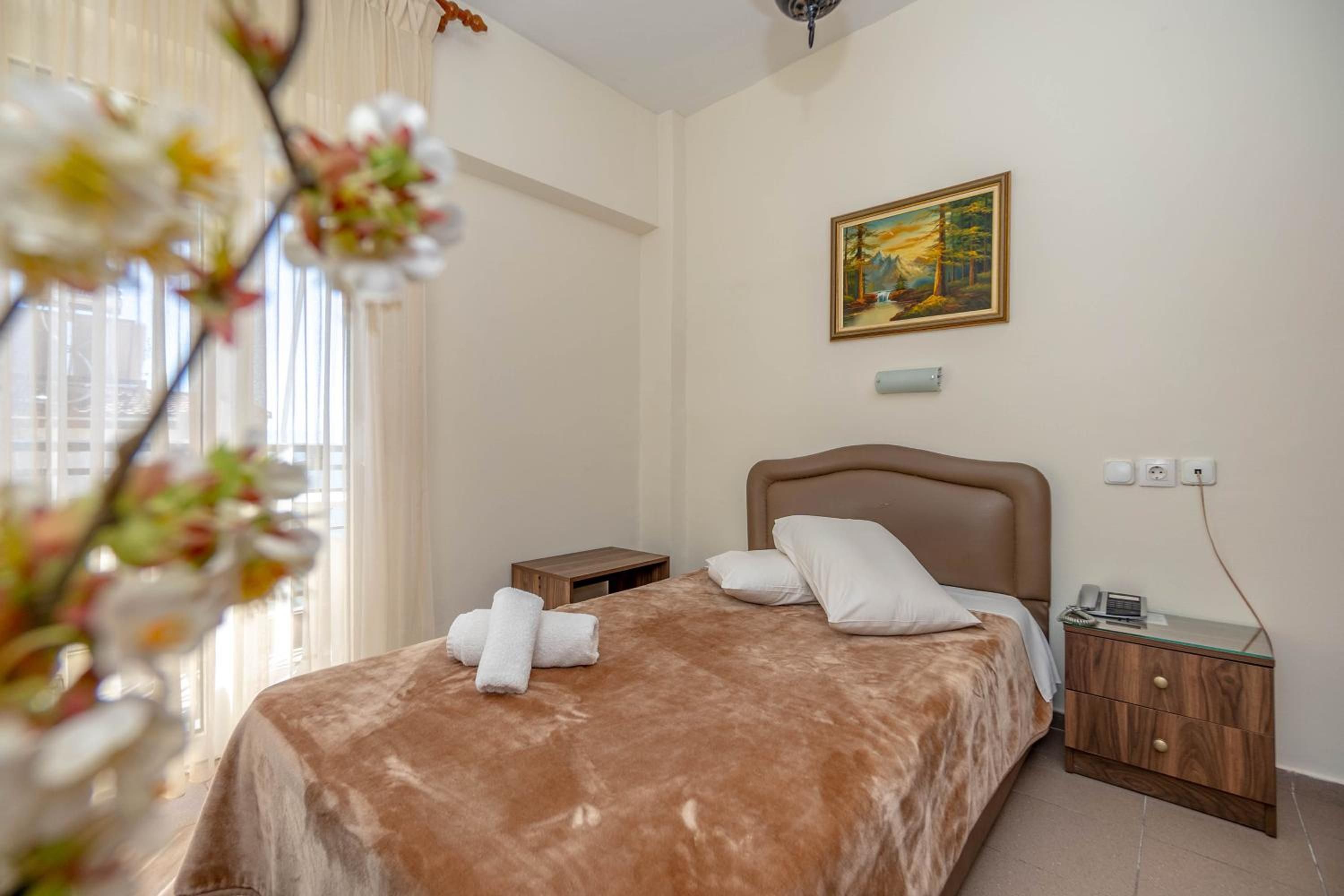 Ein Schlafzimmer mit einem Bett, einem Nachttisch, einem Gemälde und einem Fenster mit Vorhängen.