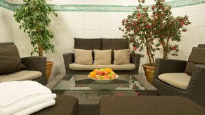 A cozy seating area with a sofa, two armchairs, and a glass coffee table with a bowl of fruit. There are two potted plants, one with green leaves and another with red flowers. - Scandic Sundsvall City (Sundsvall)