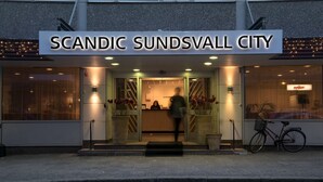 The entrance to Scandic Sundsvall City with a modern design, featuring a prominent sign, a reception desk, and potted plants. - Scandic Sundsvall City (Sundsvall)