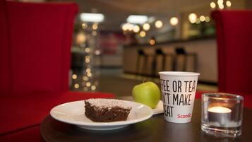 A dessert plate with a slice of cake, a green apple, a cup with text, and a candle on a table in a cozy setting.