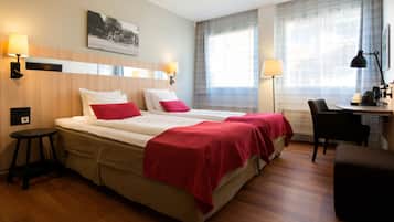 A hotel room with a double bed, two bedside tables, a desk with a chair, a lamp, and a large window with curtains.