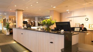 A hotel reception area with a reception desk, a large potted plant, and a clock on the wall. - Scandic Sundsvall City (Sundsvall)