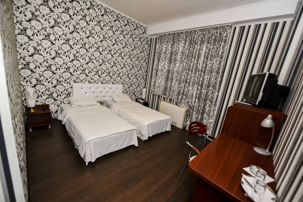 A hotel room with a large bed, a desk, a chair, a TV, and a curtain with a floral pattern.