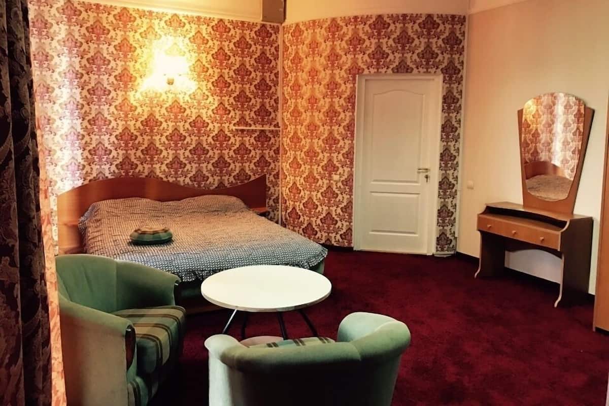 A room with a bed, two chairs, a small table, a mirror, and a door.