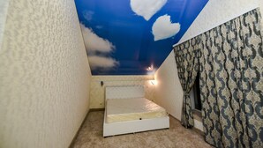 A small room with a sloped ceiling, a bed, patterned curtains, and a wall-mounted light. - Mesogios Hotel (Chisinau)
