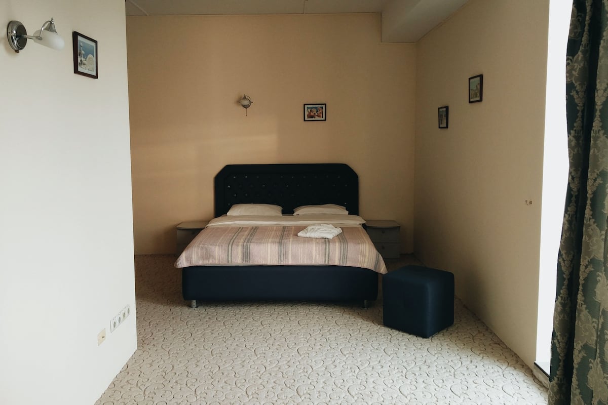A bedroom with a bed, bedside tables, a small stool, and a wall-mounted light fixture.