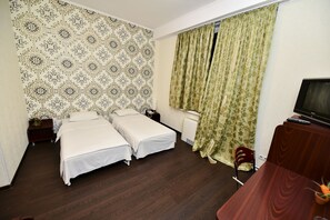 A hotel room with two beds, a wooden floor, a TV, and a desk with a chair. - Mesogios Hotel (Chisinau)