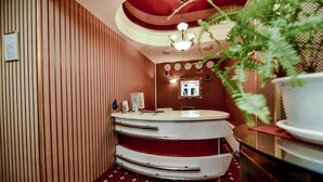 A hotel room with a curved reception desk, a red patterned carpet, a wooden panel wall, a ceiling with a red dome, and a potted plant. - Mesogios Hotel (Chisinau)