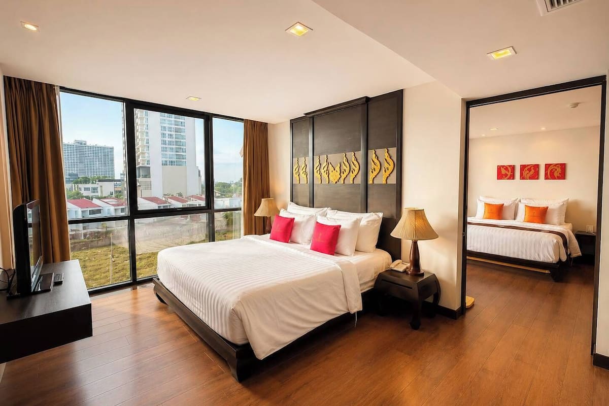 A hotel room with a large bed, a desk with a TV, and a view of the city through large windows.