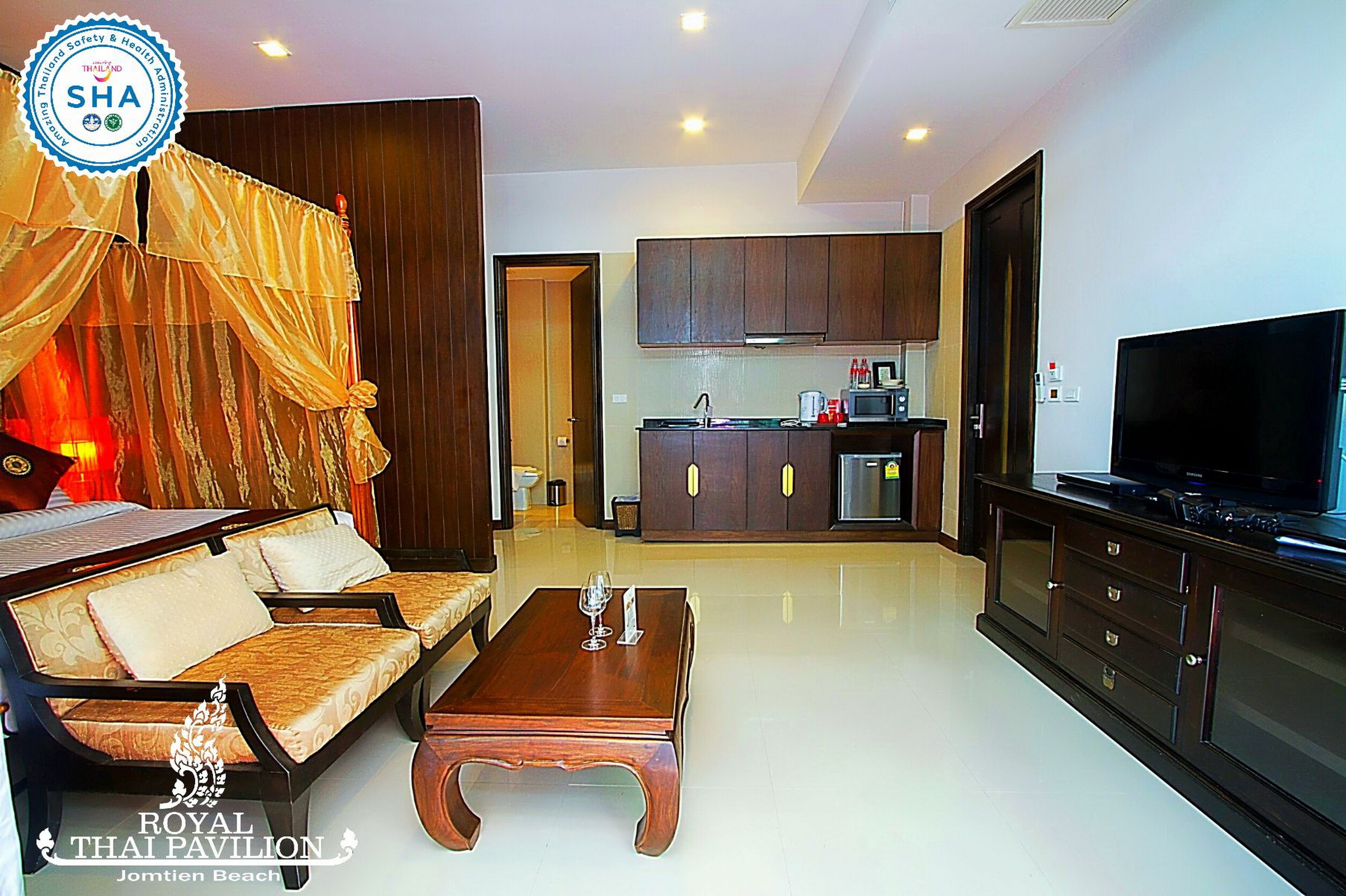 A modern living room with a sofa, coffee table, and TV. There is a kitchen area with cabinets and a microwave.