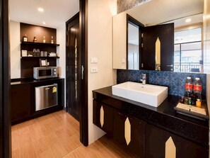 A modern bathroom with a large sink, dark cabinetry, a microwave, and a shelf with toiletries. - Royal Thai Pavilion Jomtien Boutique Resort (Pattaya)