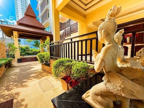 A statue of a deity in a courtyard with a tiled roof, a black marble bench, and a railing.