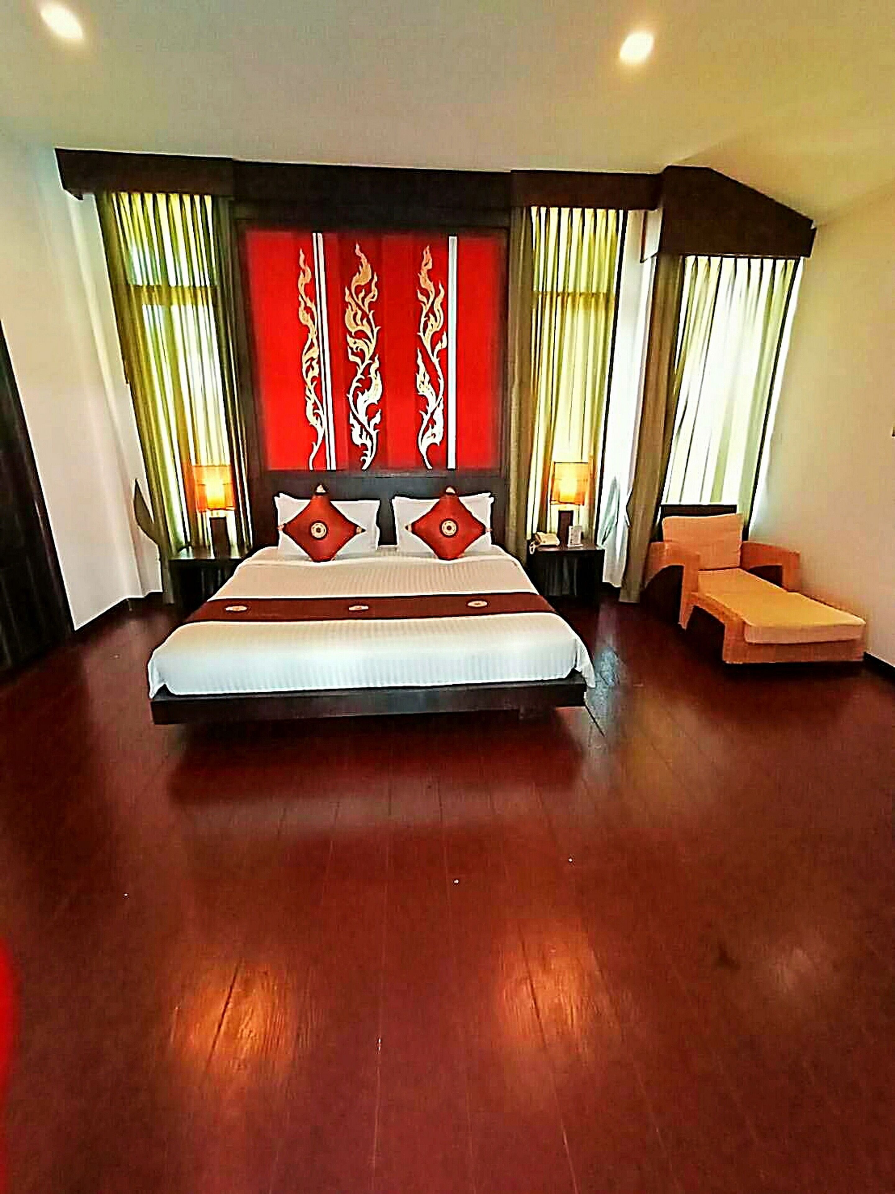 Un grand lit avec une tête de lit rouge et blanche, deux tables de chevet et un petit banc en bois.