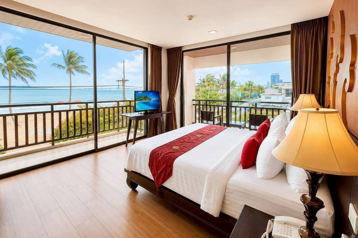 Une chambre d’hôtel dotée d’un grand lit, d’une télévision, d’un téléphone et d’un balcon offrant une vue sur l’océan et les palmiers.