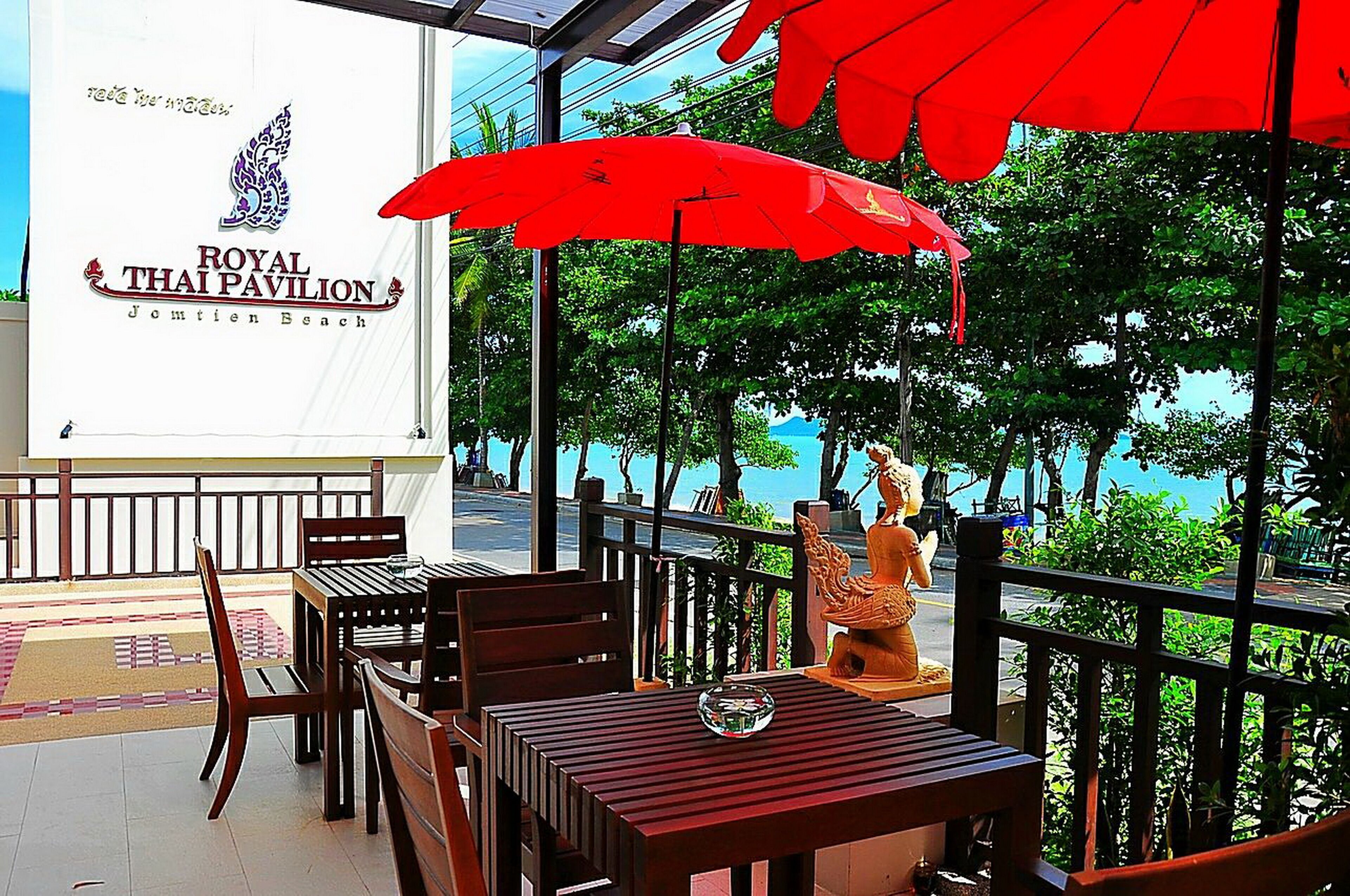 A restaurant with outdoor seating, red umbrellas, and a view of the sea.