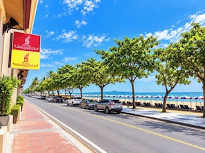 A street lined with parked cars and trees, leading to a beach with umbrellas and lounge chairs. - Royal Thai Pavilion Jomtien Boutique Resort (Pattaya)
