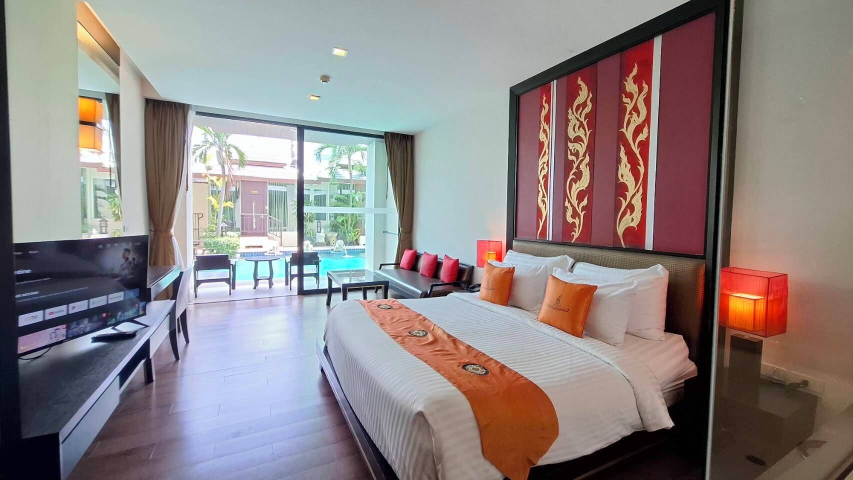A hotel room with a bed, a TV, a desk, and a view of a pool and palm trees.