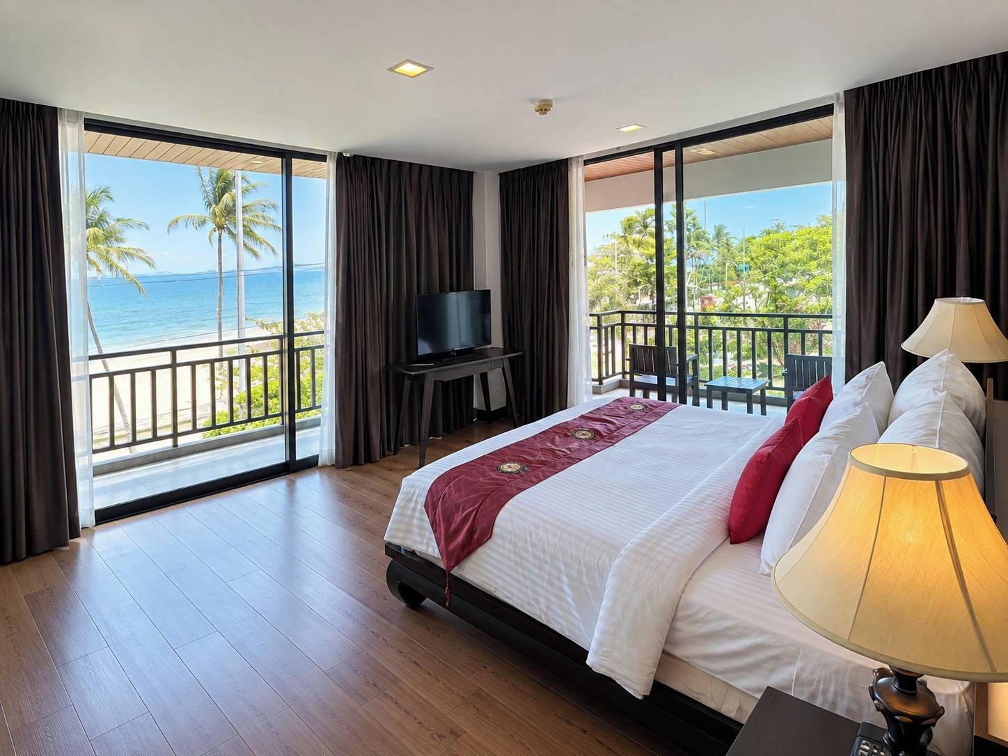 A hotel room with a large bed, a TV, and a balcony with a view of the ocean.
