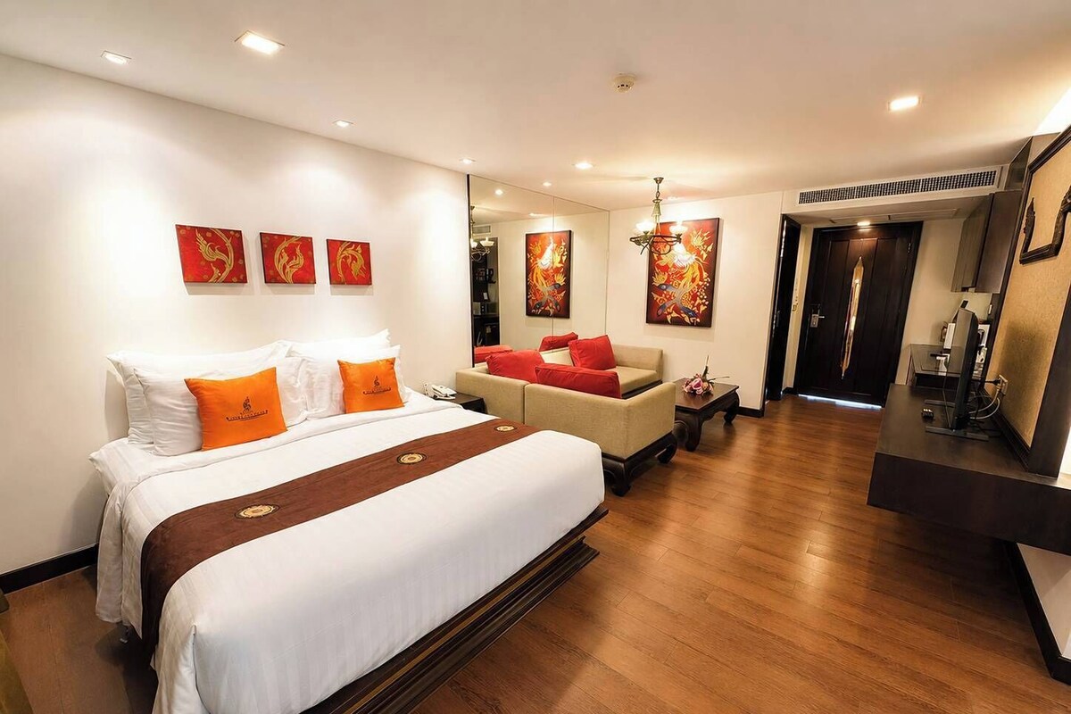 A hotel room with a large bed, a sofa, a desk, and artwork on the walls.