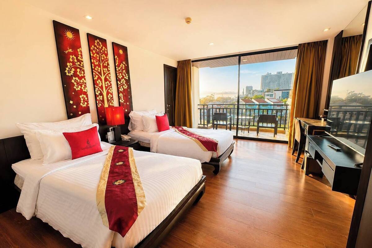 Une chambre d’hôtel avec deux lits, un bureau, une télévision et un balcon donnant sur la ville.
