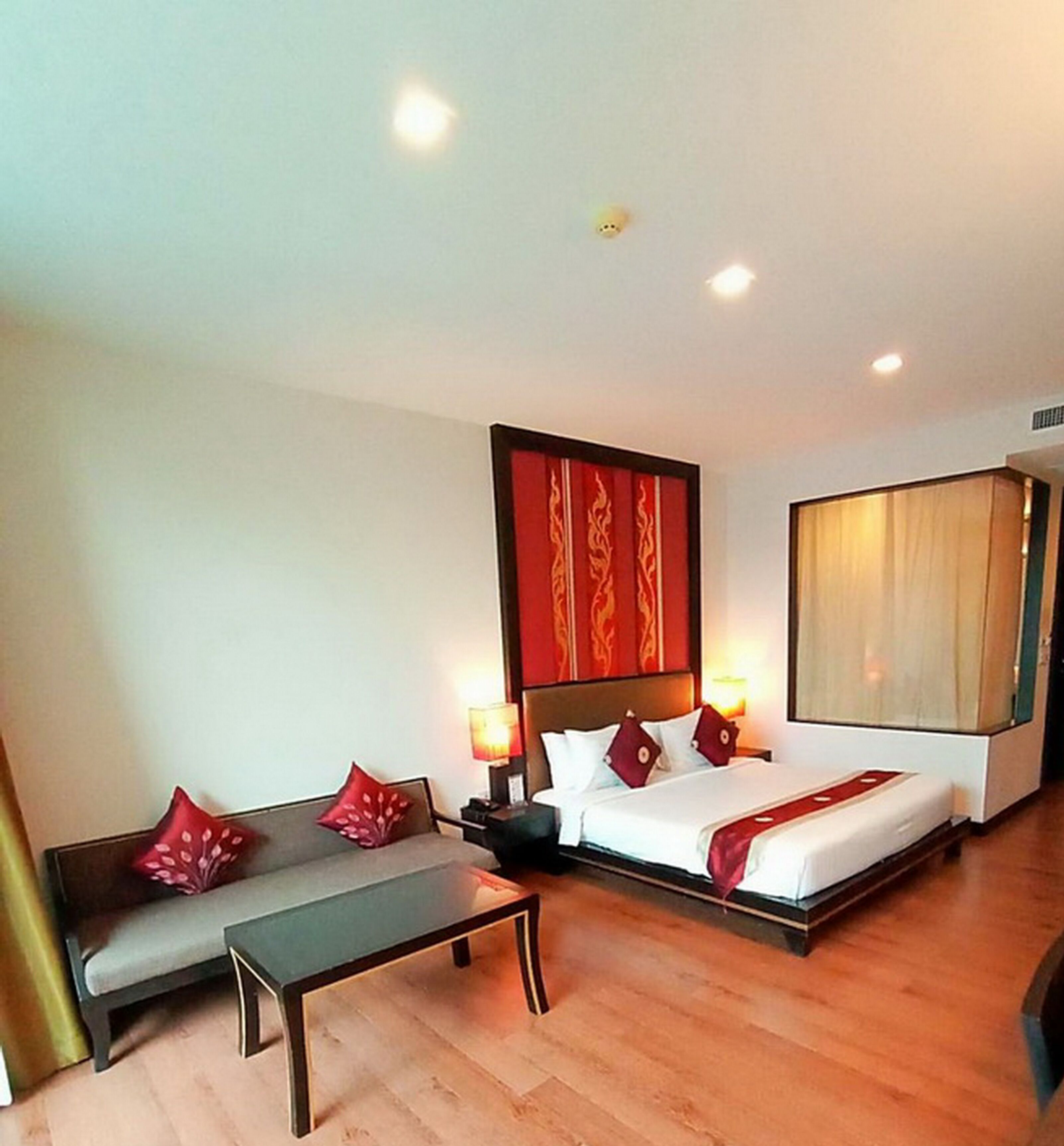 A hotel room with a large bed, a bench, and a nightstand with lamps.