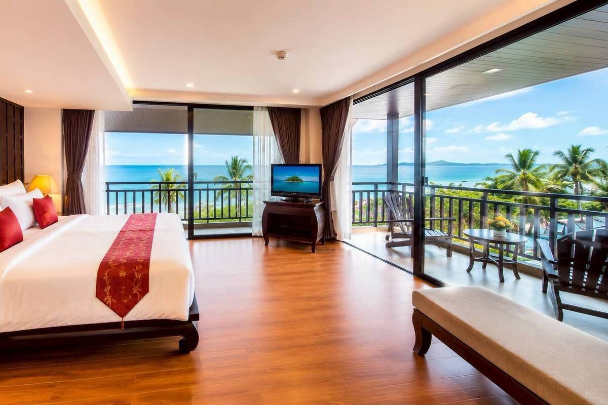 Une chambre d’hôtel comprenant un lit, une télévision, un balcon avec vue sur l’océan et un coin repas.