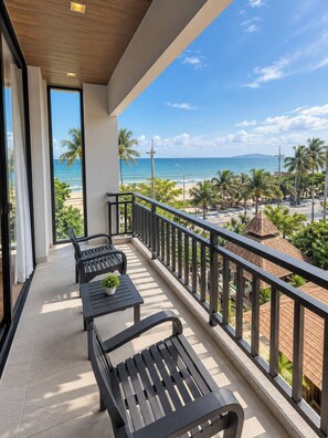 A balcony with two black benches and a small table, overlooking a beach with palm trees and a clear sky. - Royal Thai Pavilion Jomtien Boutique Resort (Pattaya)