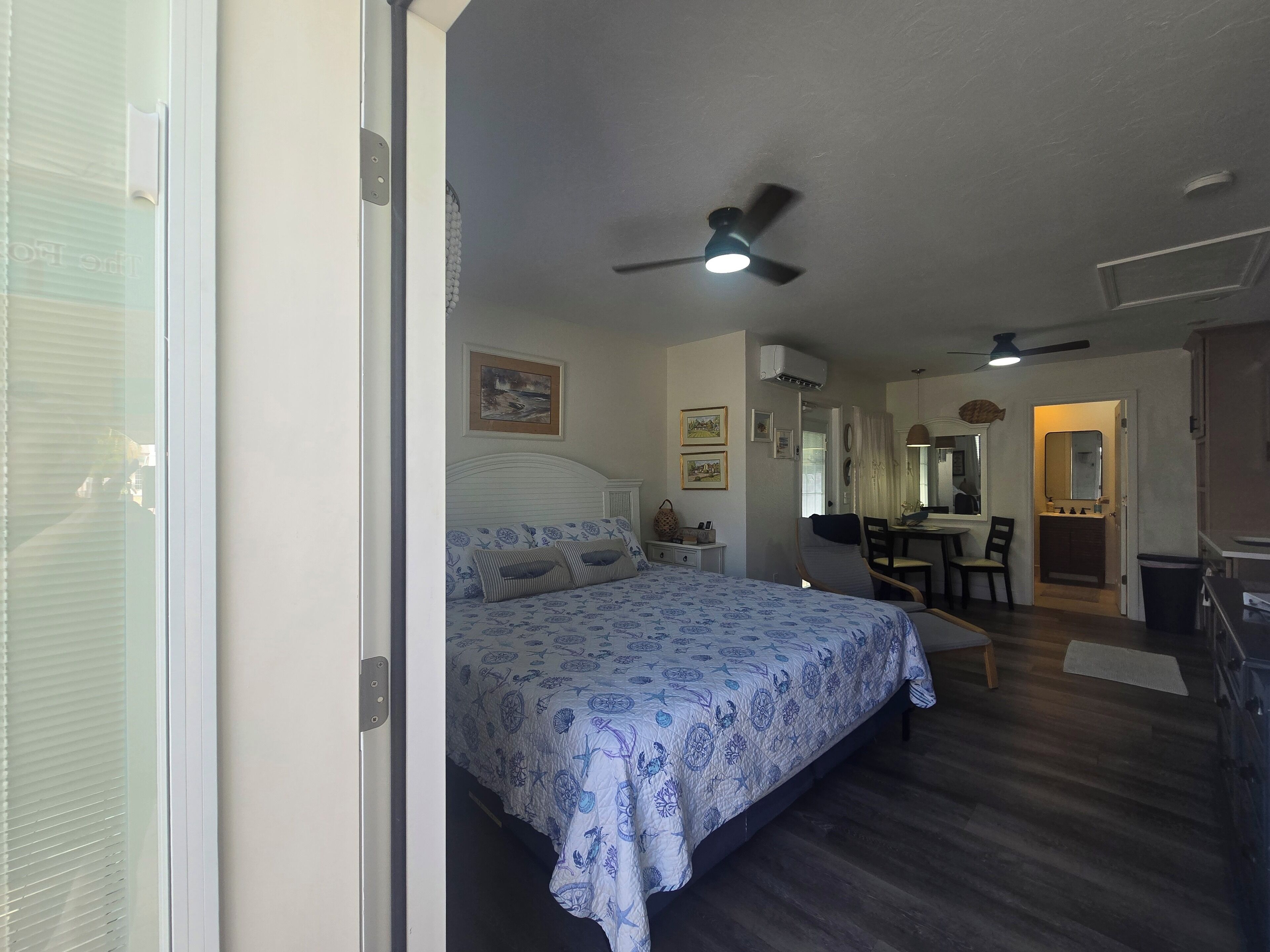 A bedroom with a bed, a ceiling fan, a desk, and a mirror.