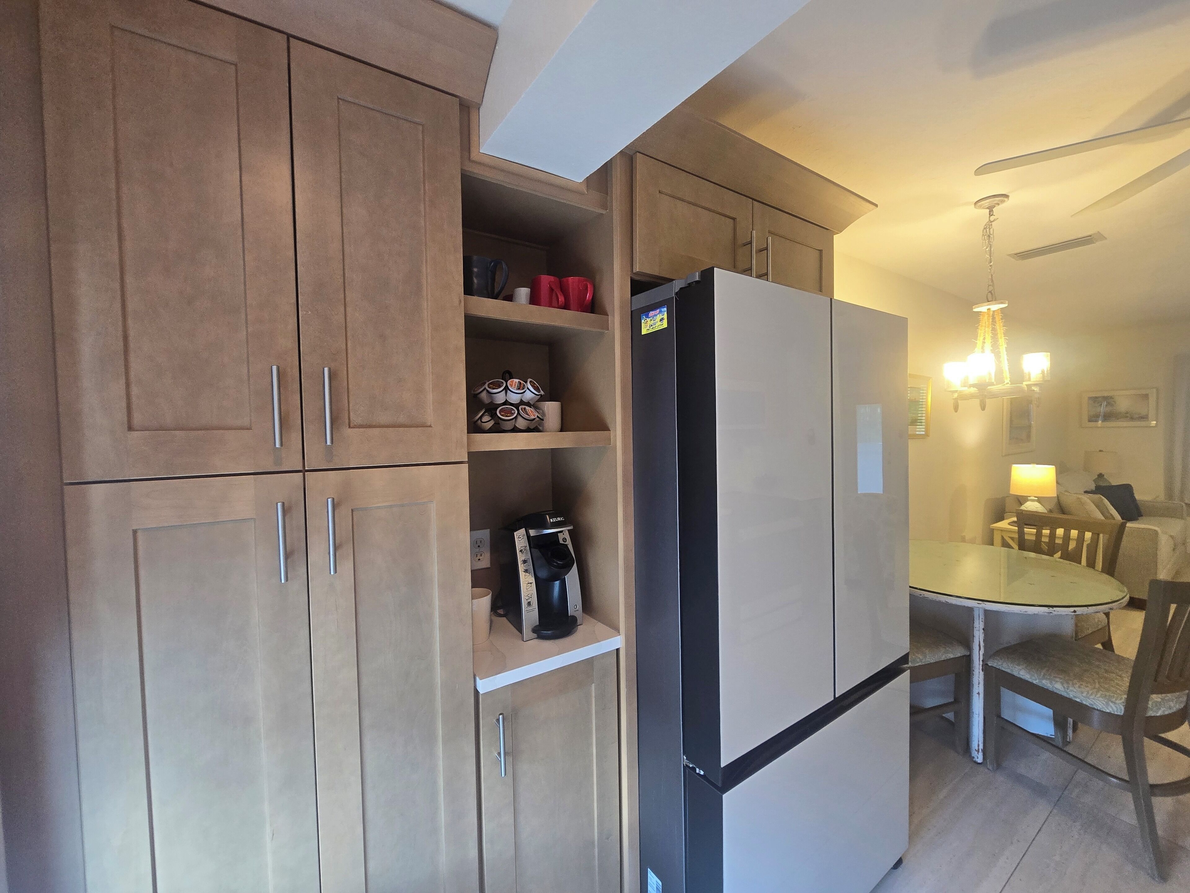 Una cucina compatta con mobili in legno, un frigorifero, una macchina per il caffè e un'area pranzo con tavolo e sedie.
