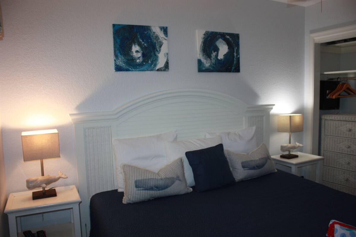 A bedroom with a bed, two nightstands, a dresser, and two abstract paintings on the wall.