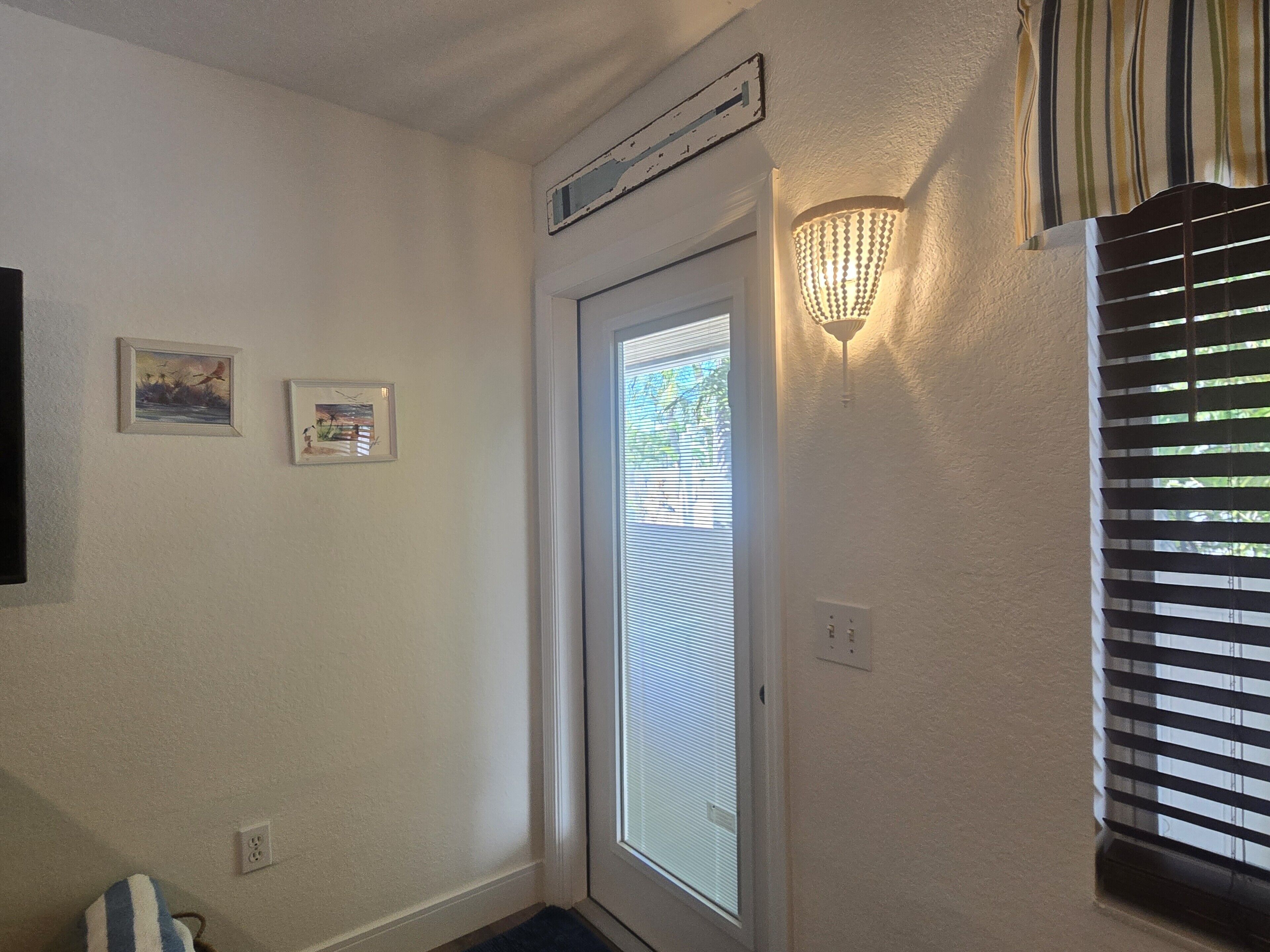 Un pasillo con una puerta, una lámpara de pared y dos cuadros enmarcados.
