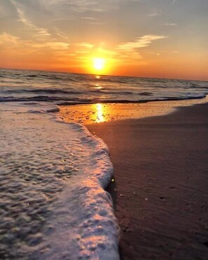 A beach scene with waves gently lapping at the shore and the sun setting in the distance. - Palm Tree Villas (Holmes Beach)