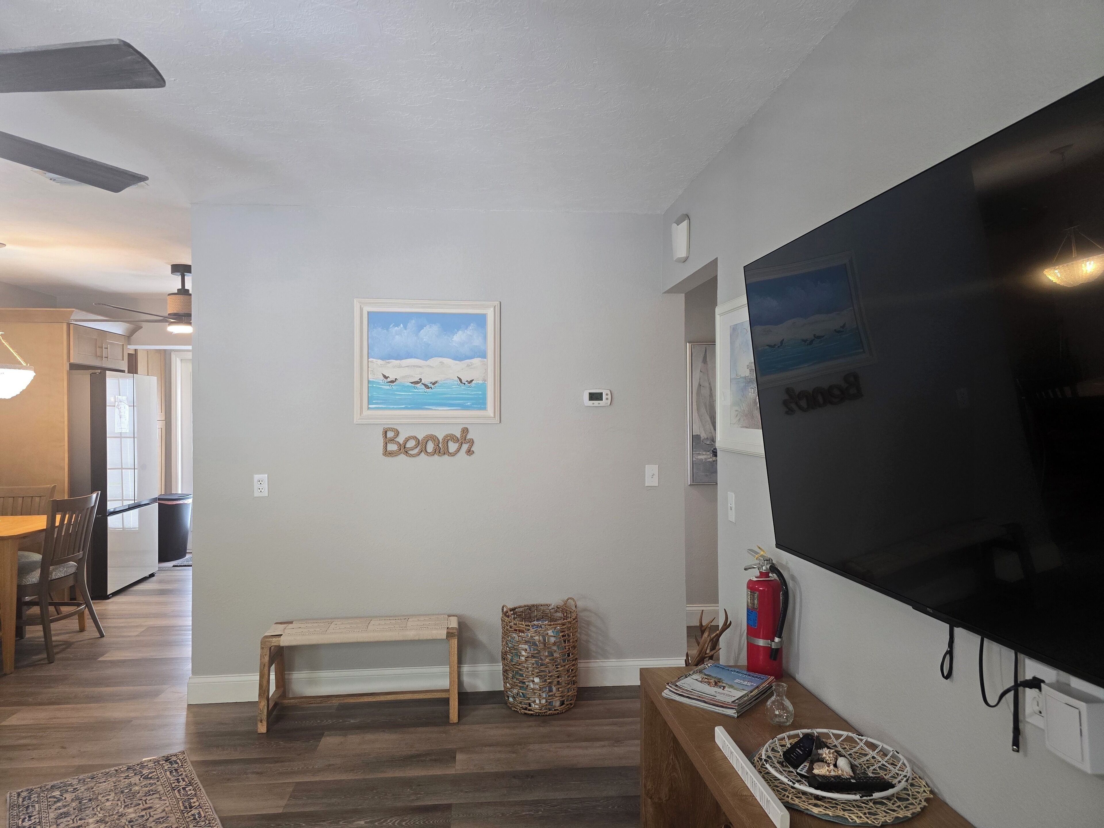 Una sala de estar con un televisor de pantalla plana grande, un cuadro enmarcados de una playa, un banco y una chimenea.