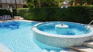 A swimming pool with a mosaic edge, lounge chairs, and a hot tub. - Hotel Tridentum (Cesenatico)