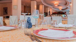 A dining table set with plates, cutlery, and glassware in a restaurant with a warm interior and elegant decor. - Hotel Tridentum (Cesenatico)