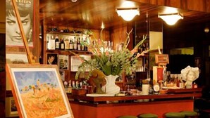 A bar area with wooden decor, a large vase with plants, and a painting on the wall. - Hotel Bacco (Camaiore)