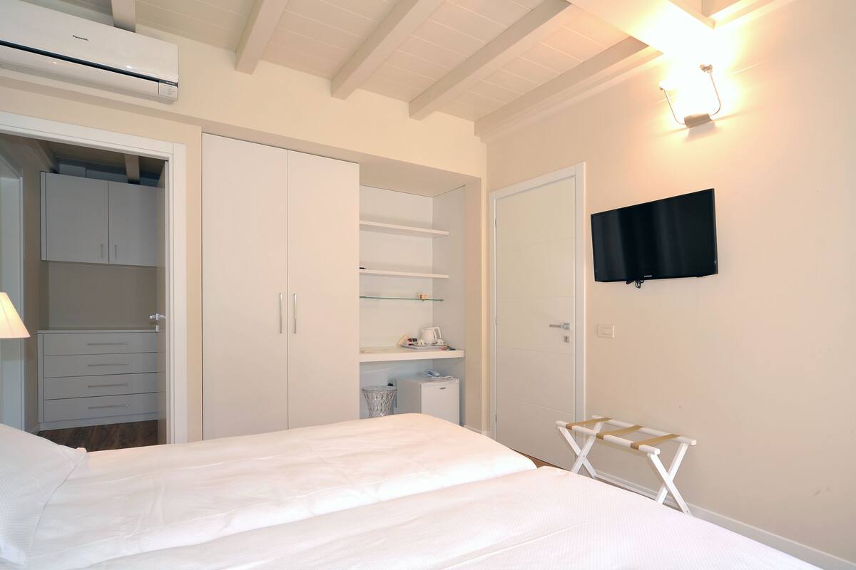 Un dormitorio con cama, armario, televisor y una mesita.