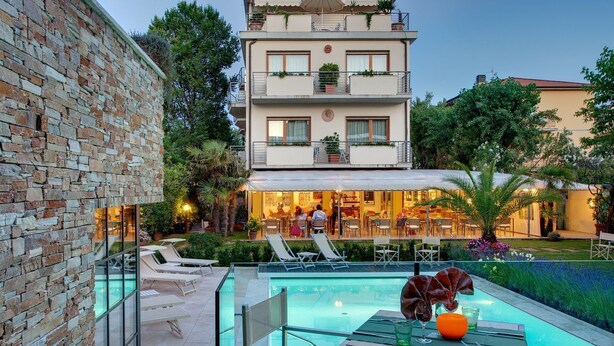 A two-story building with a pool area, outdoor seating, and a restaurant. - Hotel Bacco (Camaiore)
