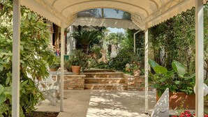 A covered garden area with a stone bench, a statue, and various plants. - Hotel Bacco (Camaiore)