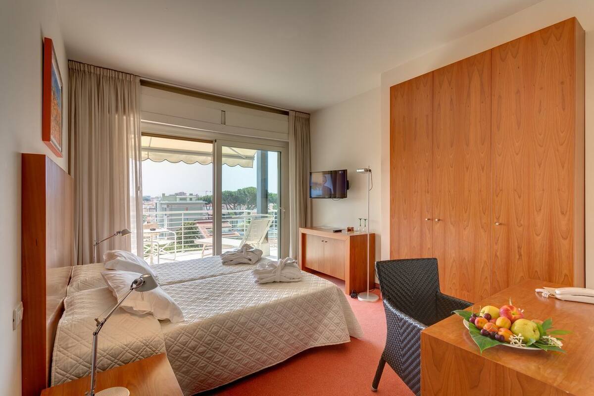 Habitación de hotel con dos camas, un escritorio, una silla y un balcón con vistas.