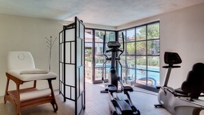 A home gym with exercise equipment, a white chair, and a view of a swimming pool through large windows. - Hotel Bacco (Camaiore)