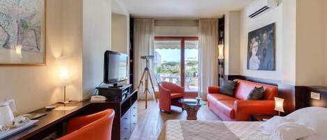 A hotel room with a bed, a desk with a computer, a chair, a sofa, and a balcony with a view.