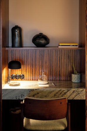 A wooden shelf with books and decorative items, a lamp, a glass dome, and a chair.