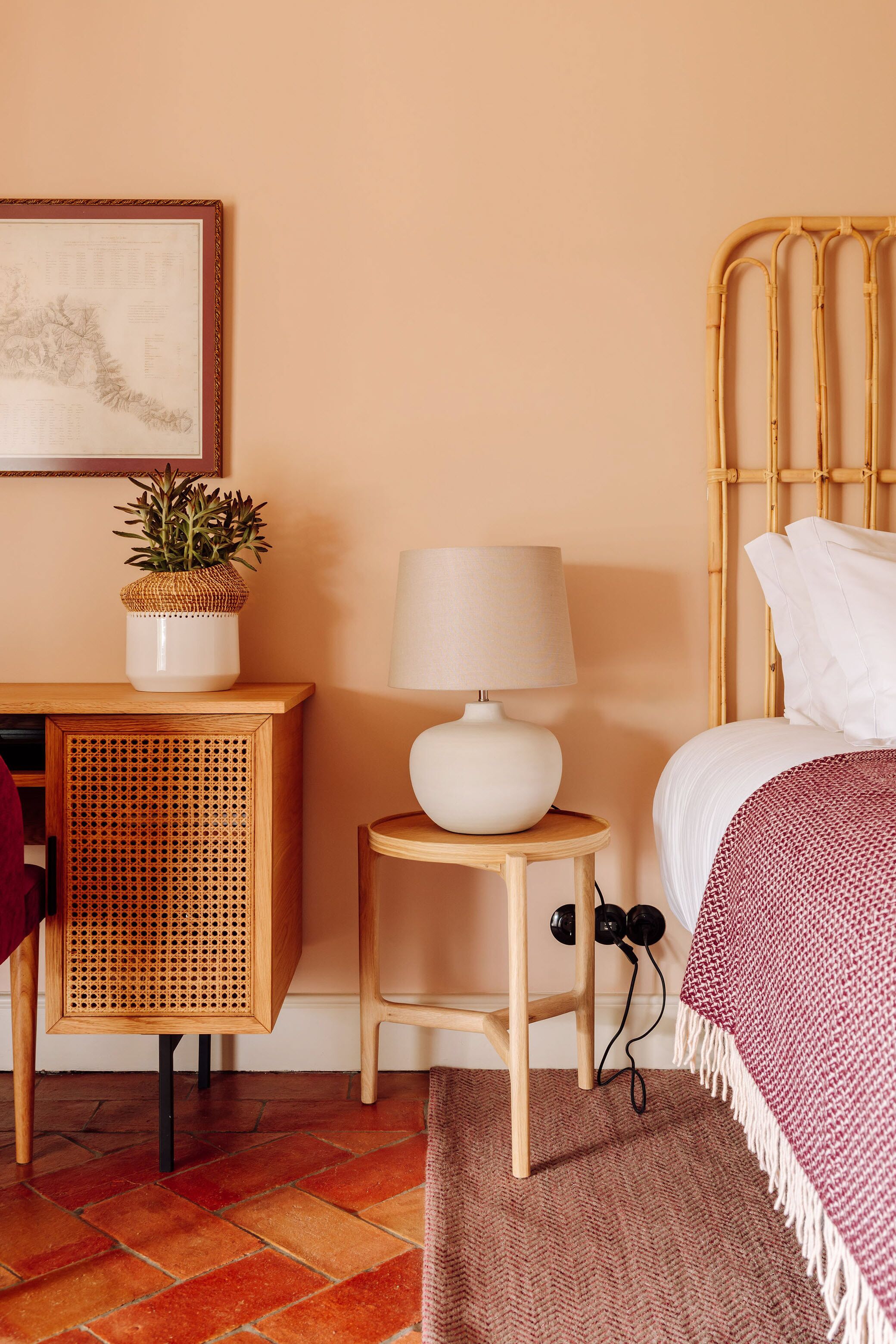 A bedroom with a bed, bedside table, lamp, and a small potted plant.