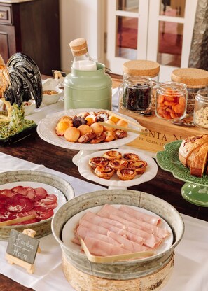 Une variété d’aliments, notamment des pâtisseries, des viandes et des pots de conserves, sont disposés sur une table en bois.