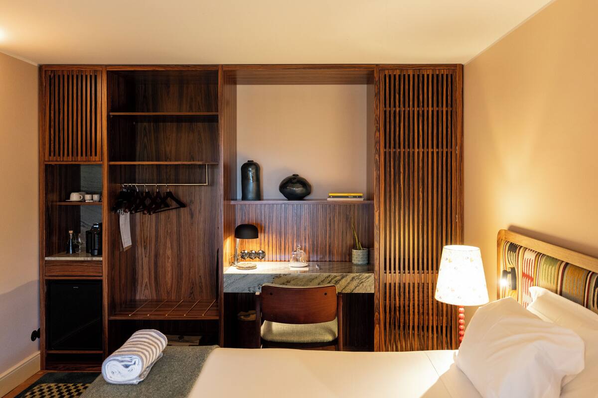 Une chambre d’hôtel comprenant un lit, un bureau, une chaise, une armoire et une petite table avec une lampe.