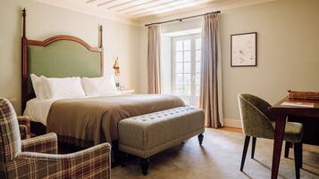 Habitación de hotel con una cama grande, un banco, una silla, un escritorio y una ventana con cortinas.